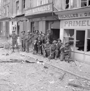 The British Army in Normandy 1944 Some of the first troops to enter Caen pose with local inhabitants outside wrecked shops, 9 July 1944.