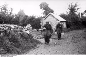 Frankreich.- Fallschirmjäger mit Raketenpanzerbüchse ("Ofenrohr" / "Panzerschreck") in Deckung hinter einem Feldstein-Mauer in einer Ortschaft vorgehend; PK Fs AOK — Frankreich