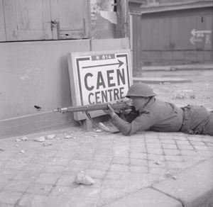 THE BRITISH ARMY IN THE NORMANDY CAMPAIGN 1944. A soldier 'keeps a sharp lookout for snipers' in the ruins of Caen, 9 July 1944. He is armed with a Lee Enfield .303 rifle and is wearing a Mk III steel helmet.