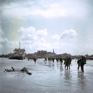 Ces soldats de l'infanterie canadienne débarquent sur la plage de Juno Beach. En arrière-plan, on aperçoit Bernières-sur-Mer. Les soldats canadiens marchent en direction de Bernières-sur-Mer.