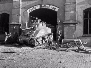 A U.S. Army M4 Sherman tank drives through the Aachen-Rothe Erde train station, Germany, in October 1944. Original caption: "The first U.S. tank to enter Aachen, Germany, rumbles through a hole opened in the railroad station by a tank-dozer. As the tanks, tank-destroyers and other heavy armament awaited the termination of a bombardment by 9th AF dive-bombers before entering Aachen, the Germans blew up a viaduct on the main avenue leading into the town."