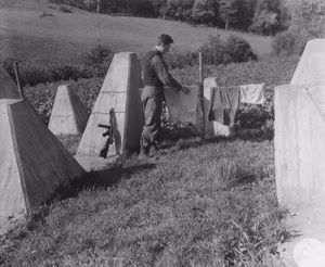 The caption reads: "What was intended to be a formidable trap for advancing allied armies turns out to be an excellent place to dry washing. PFC Anthony Mesinko, Cleveland, Ohio, uses the barbed wire of the 'impregnable' Siegfried Line to hang out his clothes."