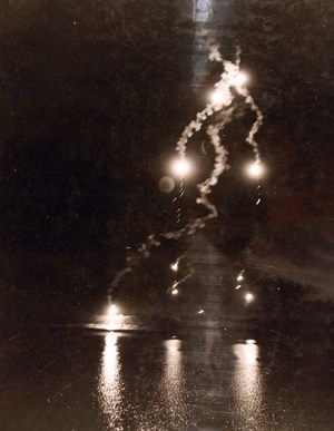 80-G-54542: Night bombing by the Axis in North Africa. Attacking some of the assembled invasion shipping at Bizerte, Axis aerial raiders lighted in the sky with flares. The beautiful display of fireworks silhouetted the shoreline. No damage was reported. Photograph, July 1943. Official U.S. Navy photograph, now in the collections of the National Archives. (2016/07/19).