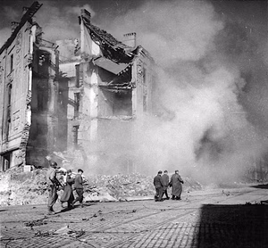 Nazi troops captured in blazing Aachen. An infantryman of the First U.S. Army (left) escorts five German prisoners along a street of blazing Aachen, Reich border city where the Nazi garrison refused to surrender. During the first 13 days of their assault against Aachen, American soldiers captured approximately 9,000 Nazis. War pool photo, not for use in British isles or Western hemisphere. Serviced by London OWI to list B. Certified as passed by SHAEF censor.