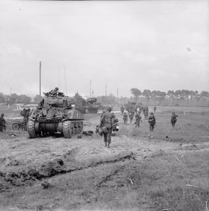 D-day - British Forces during the Invasion of Normandy 6 June 1944 Infantry of 3rd Division move inland from Queen beach, Sword Area, past a Sherman tank of 27th Armoured Brigade, 6 June 1944. In the background M10 3-inch self propelled guns can be seen.