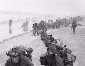D-day - British Forces during the Invasion of Normandy 6 June 1944 Troops of 3rd Infantry Division on Queen Red beach, Sword area, circa 0845 hrs, 6 June 1944. In the foreground are sappers of 84 Field Company Royal Engineers, part of No.5 Beach Group, identified by the white bands around their helmets. Behind them, medical orderlies of 8 Field Ambulance, RAMC, can be seen assisting wounded men. In the background commandos of 1st Special Service Brigade can be seen disembarking from their LCI(S) landing craft.