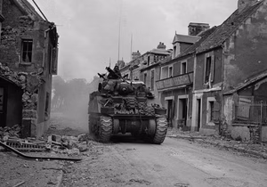 Canadian Army M4 Sherman tank moving through the war-torn city of Caen, France. Photograph captured on July 10, 1944, during the Allied advance in Normandy. The tank is identified as belonging to the Sherbrooke Fusiliers of the 2nd Canadian Armoured Brigade.