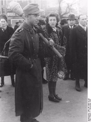 For documentary purposes the German Federal Archive often retained the original image captions , which may be erroneous, biased, obsolete or politically extreme . Budapest November 1944 Für 30 Filler in die Hauptkampflinie! Hinter dem starken Speergürtel, den deutsche und ungarische Einheiten um die Hauptstadt Budapest gelegt haben, geht das Leben unbehindert weiter. Nur wenige Kilometer von der Stadt entfernt zieht sich die Hauptkampflinie entlang, an der sich die Bolschwisten immer wieder blutige Köpfe holen. Mit der normal verkehrenden Strassenbahn kann man bis zu den rückwärtigen Posten der Sicherungslinie fahren, ein Zustand, der wohl einmalig in der Geschichte dieses Krieges ist. Mit der Panzerfaust bewaffnet, warten Grenadiere neben Zivilisten an der Haltestelle. SS-PK- F. Fritsch