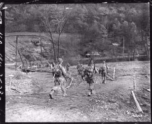 Deep in the Hurtgen forest, in Germany, American infantrymen move across a bridge over a small stream. A tank, part of the new Allied offensive, can be seen in the background.