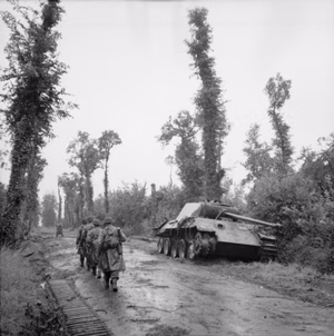 The British Army in Normandy 1944 Infantry of 2nd Battalion, Essex Regiment file past a knocked out German Panther tank on a road near Tilly-sur-Seulles, 19 June 1944.