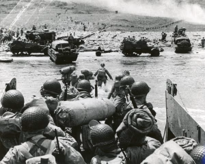 American troops landing at Omaha Beach, June 6, 1944. The presence of tracked vehicles and DUKWs (“Ducks”) on the beach and the organized columns of men heading inland indicate that this photo was taken several hours after the initial infantry assault.