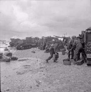 D-day - British Forces during the Invasion of Normandy 6 June 1944 3rd Division troops sheltering behind Universal Carriers (one with a towed 6-pdr AT gun) on Queen beach, Sword area, 6 June 1944. An M10 Wolverine 3-in self-propelled gun and a Bofors anti-aircraft gun can be seen in the background.