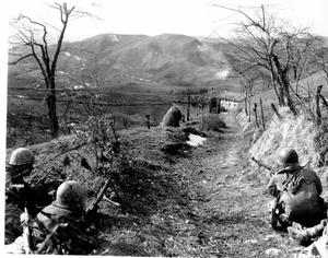 A machine gunner and two riflemen of Co K, 87th Mountain Infantry, 10th Mountain Division, cover an assault squad routing Germans out of a building in the background. Sassomolare Area, Italy. Porretta Moderna Highway. 4 March 1945.