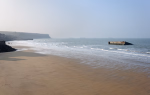 The beach of Arromanches-les-Bains in Normandy, France, with the remains of the portable temporary Mulberry harbour in the water.