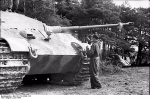 Frankreich.- Soldat beim Besprühen eines Panzer VI "Tiger II" (Königstiger) mit Farbe (?), im Hintergrund PKW unter Bäumen stehend; PK KBZ OB West — Frankreich