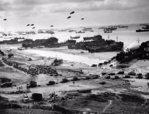 Landing ships putting cargo ashore on Omaha Beach at low tide during the early days of the Allied invasion, mid-June 1944. Among identifiable ships present are LST-532 (in the center of the view); USS LST-262 (3rd LST from right); USS LST-310 (2nd LST from right); USS LST-533 (partially visible at far right); and USS LST-524. Note barrage balloons overhead and U.S. Army "half-track" convoy forming up on the beach. The LST-262 was one of 10 Coast Guard-manned LSTs that participated in the invasion of Normandy, France.