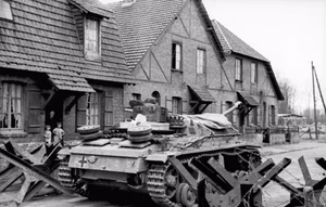 Nordfrankreich.- Sturmgeschütz III fährt durch Panzersperre vor Fachwerk-Gebäude; PK 698 — Nordfrankreich