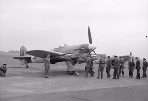 Royal Air Force- 2nd Tactical Air Force, 1943-1945. King George VI and his entourage of senior RAF officers walk over to Hawker Typhoon Mark IB, MN454 'HF-S', of No. 183 Squadron RAF, while inspecting aircraft and equipment which will be used in the forthcoming invasion of Normandy at Northolt, Middlesex. MN454 was flown by the Commanding Officer of 183 Squadron, Squadron Leader the Hon. F H Scarlett. Behind the King's party is a Supermarine Spitfire Mark IX of No. 222 Squadron RAF.