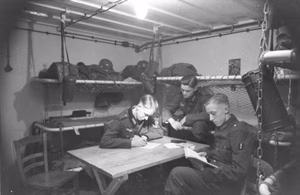 Im Westen.- Bunker an der Oberrheinfront an einem Fluss.- drei Soldaten, darunter Schütze der Nachrichtentruppen, im Inneren (Mannschaftsquartier) am Tisch sitzend, lesend; PK 670 — Im Westen