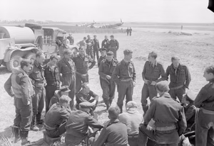 Royal Air Force- 2nd Tactical Air Force, 1943-1945. Hawker Typhoon pilots of Nos. 121 and 124 Wings discuss operations at B2/Bazenville, Normandy, on the evening of 14 June 1944. In the foreground, standing on the left, are five pilots of No. 175 Squadron RAF, including the Commanding Officer, Squadron Leader M R Ingle-Finch (fourth from left): on the right stand members of No. 181 Squadron RAF with their commander, Squadron Leader C D 'Kit' North-Lewis sitting on the far right. In the farthest group, those identified include Wing Commander C L Green (wearing helmet) leader of No. 121 Wing, and Squadron Leader W Pitt-Brown, commander of No. 174 Squadron RAF (on the right, wearing a lanyard). In the background, Supermarine Spitfire Mark IXs of No. 66 Squadron RAF stand at their dispersal points.