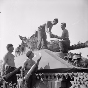 A Sherman Firefly crew of 1st Northamptonshire Yeomanry load ammunition for the 17-pounder gun into their vehicle before the start of Operation 'Totalise' .