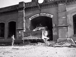 A U.S. Army M4 Dozer tank drives through the Aachen-Rothe Erde rail station, in October 1944. Original caption: "While 9th AF fighter-bombers were attacking strongpoints in the city of Aachen, Germany, preparatory to an assault by ground troops, the German defenders blew up a viaduct leading into the town. How the Americans circumvented the enemy demolition is shown in this photograph of a tank-dozer smashing through the railroad station adjacent to the viaduct. A few minutes later the first U.S. tanks and ground troops entered the city."
