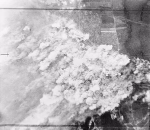 Royal Air Force Bomber Command, 1942-1945. Vertical aerial photograph showing smoke from exploding bombs smothering the Colombelles steelworks, east of Caen, France during the attack by aircraft of Bomber Command in support of the Second Army's armoured advance in the Normandy battle area, (Operation GOODWOOD).